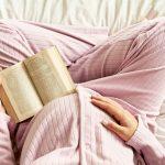 Pregnant mom sitting on bed reading - World Health Day | Latina Mom Collective