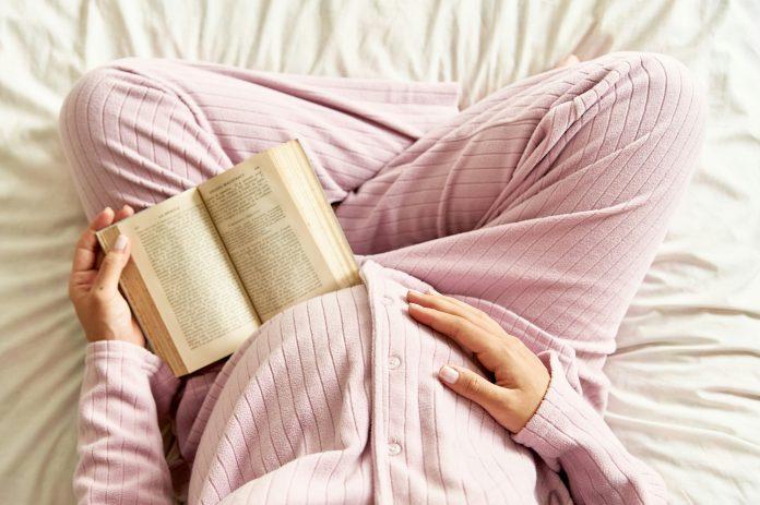 Pregnant mom sitting on bed reading - World Health Day | Latina Mom Collective