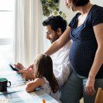 dad holding tablet, mom and daughter looking on | raising kids away from family