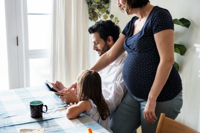 dad holding tablet, mom and daughter looking on | raising kids away from family