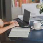 woman working on laptop, coffee next to computer and open notebook | Latina working mom balance