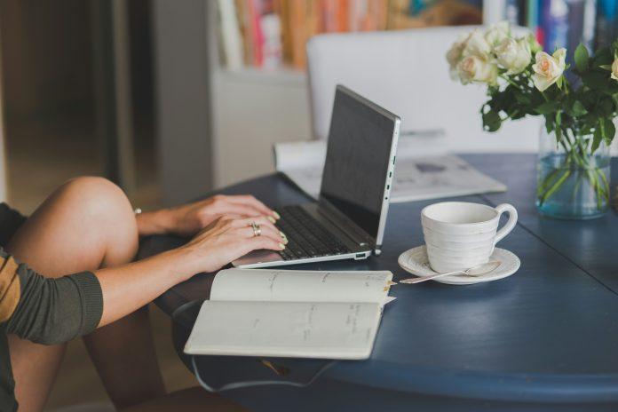 woman working on laptop, coffee next to computer and open notebook | Latina working mom balance