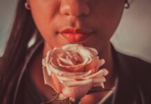 February, But Make It Paquita & Jenni Woman with red lips holding pink rose in front of her face | February, but make it Paquita & Jenni