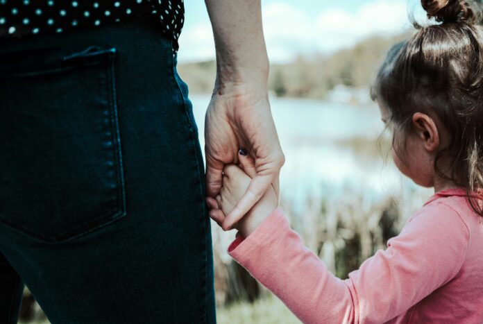 mom holding child's hand while looking out at pond
